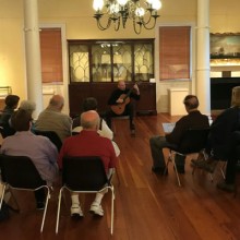 Musician playing guitar to a room full of listeners