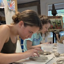 two young female ceramic students work at a table