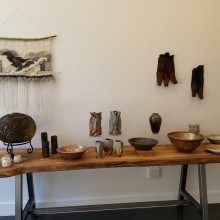 a collection of artworks on a wooden desk, among them earth tone colored ceramic bowls, etched wood art, and yarn art