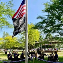 Imperial Brass performing outside beneath an American flags and a POW flag