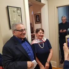 Two older adults smiling while someone photographs them on their phone