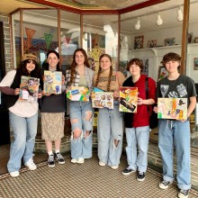 group photo of teens holding up their artwork in front of an art studio