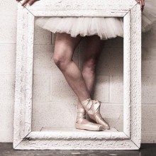 Ballerina wearing a tutu and pointe shoes posing behind a frame. Photo by Brian Mengini
