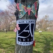 Fair Lawn Arts Council logo knitted and posted on a tree, along with a knitted butterfly