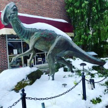 Snow covered dinosaur sculpture in front of a building