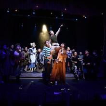 a performance of Les Mis onstage with two men holding up a boy