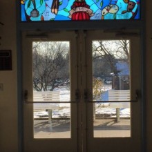 A view through pair of double doors with a stained glass window looking out onto a snowy day