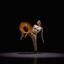 Dancer onstage, right leg bent and raised, holding a sombrero.