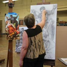 woman painting a black and white image on a canvas sitting on an easel