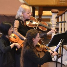 image of three women playing violins in all black clothing