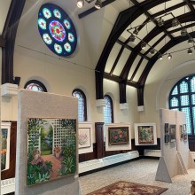 floral landscape paintings displayed in large room with arched ceilings and stained glass windows