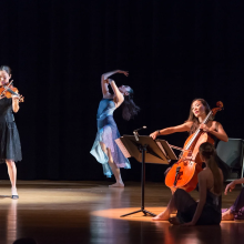 A group of dancers on stage with violins and cellos