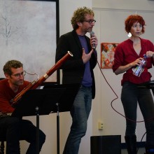 A trio of musicians between songs, performing respectively with an oboe a piano and a microphone
