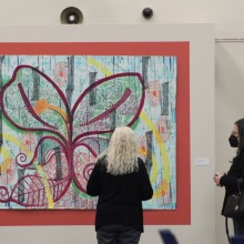 Two women look at a large painting of a butterfly in an art gallery