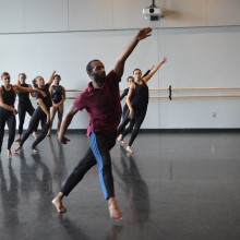 an instructor leads a group of girls across the floor in a dance move