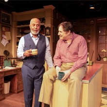 Two men sitting on top of a kitchen counter acting in a play