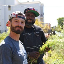 two men smiling holding some herbs an outdoor garden