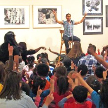 Storyteller in front of a gallery wall before an audience of children.