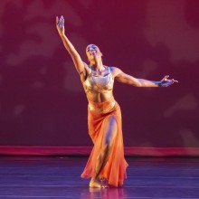 An African American dancer from Philadnco in a gold and orange sheer costume posing on Pfleeger stage, about to curtsy