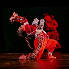 Performer dressed in bright red posed in a dance move on stage.