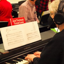 A woman is playing a piano in a class with other adult students.