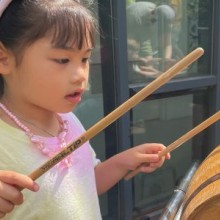 A little girl playing a drum in front of a barrel