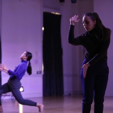 Two dancers performing in a darkened room with purple lighting.