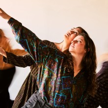 Two dancers posed in the foreground with a group of dancers blurred in the background.