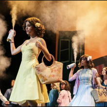 Cast performing in "Hair Spay" holding cans of aerosol.