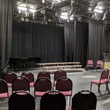 A large black box theatre with rows of event chairs and a stage.