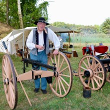 A man in period clothing standing next to two wooden cannons.