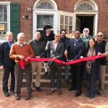 A group of people cutting a red ribbon in front of a brick building.