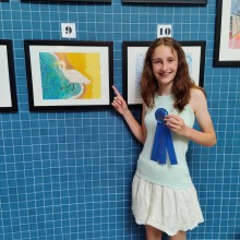 A girl holding a blue ribbon in front of framed artwork at the Ocean City Arts Center