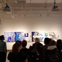 A group of people in front of a series of art panels on a gallery wall