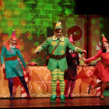 Actors onstage wearing elf costumes on a holiday themed set.
