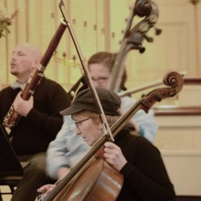 A wo man wearing a hat playing a cello in an orchestra.