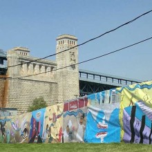 A mural on a fence with the Benjamin Franklin Bridge in the background.