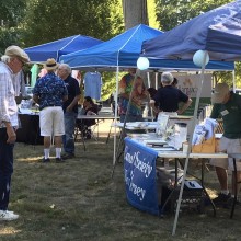 Farmers market with blue pop up tents and people sitting at tables.