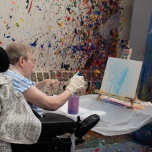 An artist with a disability in front of their work in progress.