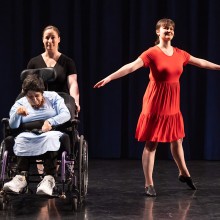 Performers standing and in a wheelchair on a stage.