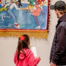 A father and daughter look at art work on a gallery wall.