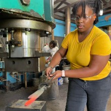 A woman in a yellow shirt working in a metal shop