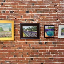 A group of framed art pieces and fiber art pieces on a brick wall.