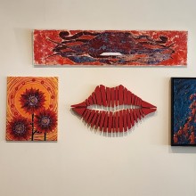 A group of framed art pieces and fiber art pieces on a wall.