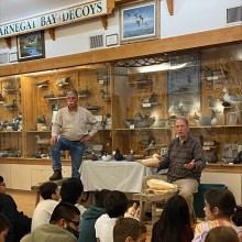Two men talking in front of a display of decoy ducks.