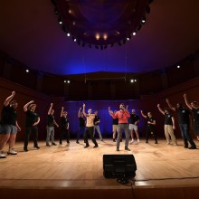 A group of performers rehearsing on stage in a semi-circle.