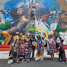 A group of Indigenous artists posing in front of a mural