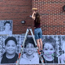 Mural installation of black and white photographs on a red brick wall.