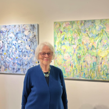 Woman at art exhibition in front of colorful paintings.