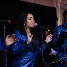 A group of people in sparkly blue suits singing into microphones on stage.